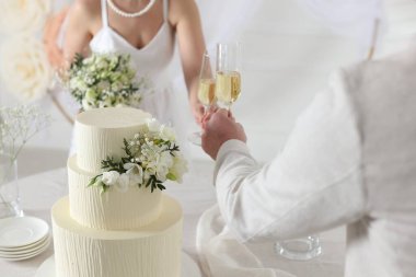 Evde düğün pastası olan evli bir çift şampanya bardaklarını tokuşturuyor.