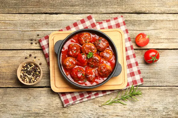 Fırın tabağında domates soslu leziz köfteler ve ahşap masada baharatlar.