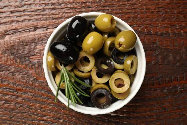 Farklı lezzetlerde marine edilmiş zeytin halkaları, bütün halkalar ve biberiyeler ahşap masada, üst tarafta.