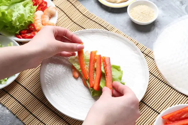 Açık gri masada nefis börek yapan bir kadın.