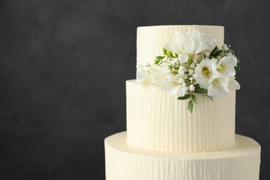 Gri arka planda çiçek dekoru olan lezzetli düğün pastası, yakın plan. Metin için boşluk