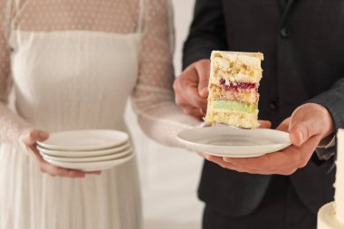 Damat, düğün pastasının bir parçasını tabağa koyuyor. Gelini içeride tutuyor, yakın plan.