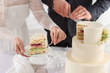 Yeni evliler kapalı bir masada düğün pastası kesiyorlar.