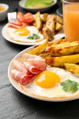 Lezzetli bir kahvaltı. Koyu dokulu masada kızarmış yumurta, patates ve pastırma, yakın plan.