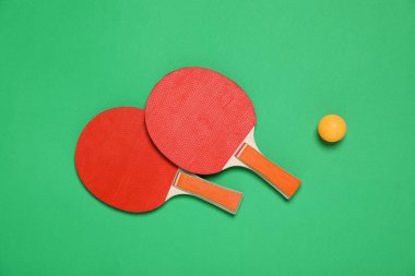 Yeşil arka planda pinpon raketleri ve top düz yerde. Spor malzemeleri.