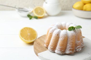 Beyaz ahşap masada pudra şekerli, nane ve narenciye meyveli lezzetli limonlu pasta, yakın plan.