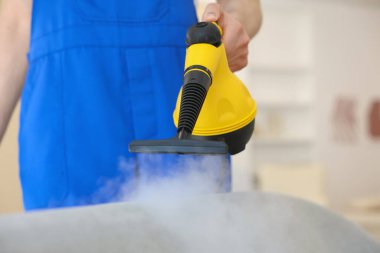 Temizlikçi kanepeyi evde buharlı temizleme makinesiyle temizliyor.