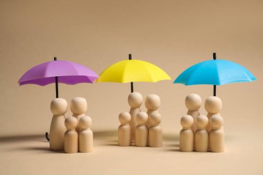 Bej arka planda şemsiye altında insan figürleri. Sigorta konsepti