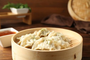 Bambu tenceresinde kaynamış gyoza (hamur tatlısı) ve ahşap masada sos, yakın plan.