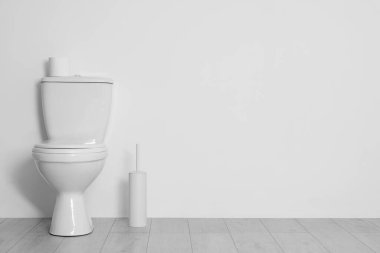 Toilet, brush and paper near white wall. Space for text