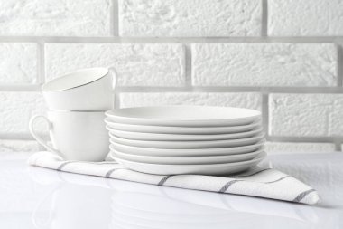 Different clean dishware on white table near brick wall