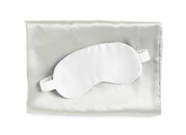 Beyaz arka planda ipek çarşaflar ve uyku maskesi, üst manzara.