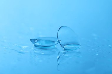 Açık mavi ayna yüzeyine bir çift kontak lens ve su damlası, yakın plan.