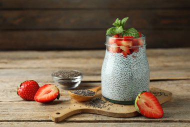 Çilekli lezzetli chia pudingi ve ahşap masada cam kavanozda nane şekeri.