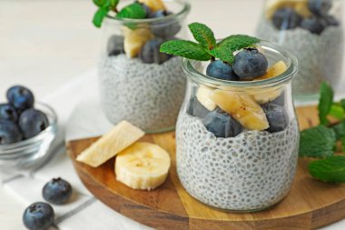 Yaban mersinli lezzetli chia pudingi, muzlu ve naneli bardaklar ışıklı masada, yakın plan.