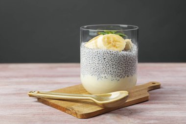 Muz ve nane aromalı lezzetli chia pudingi ahşap masada gri arka planda servis edilir.