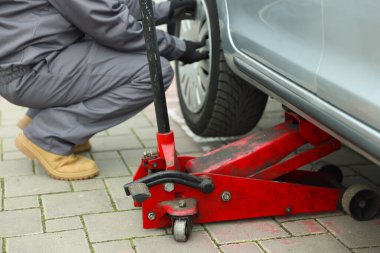 Makas kriko ile kaldırılan araba. Otomatik tamirci dışarıdaki tekerleği değiştiriyor, yakın plan.