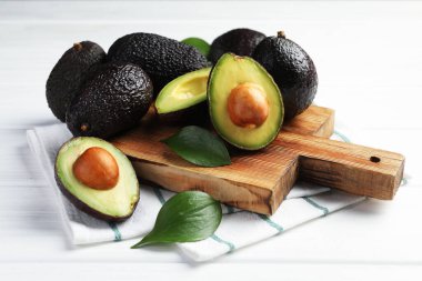 Avokadolar ve yapraklar beyaz ahşap masada, yakın plan.