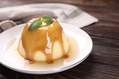 Karamel soslu lezzetli puding ve ahşap masada nane şekeri, yakın plan.
