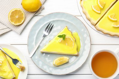 Beyaz ahşap masada servis edilen limon kaymaklı leziz peynirli kek.