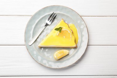 Beyaz ahşap masada servis edilen limonlu peynirli kek.