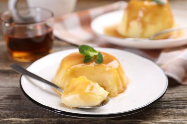 Karamel soslu lezzetli puding ve ahşap masada servis edilen nane, yakın plan.