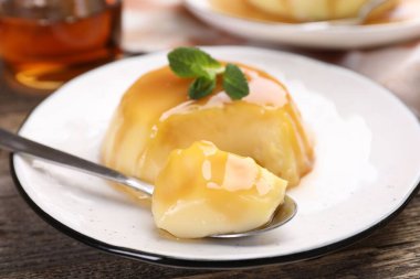 Karamel soslu lezzetli puding ve ahşap masada servis edilen nane, yakın plan.