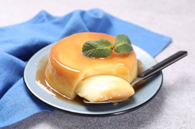 Karamel soslu lezzetli puding, gri desenli masada nane ve kaşık, yakın plan.
