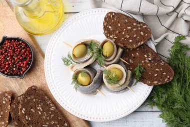 Beyaz ahşap masada servis edilen zeytinli lezzetli ringa dürümleri.