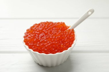 Lezzetli kırmızı havyar kasede ve kaşık beyaz ahşap masada, yakın plan