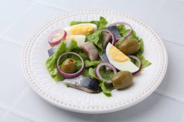 Ringa balıklı lezzetli salata, yumurta ve sebzeler beyaz fayanslı masada, yakın plan.