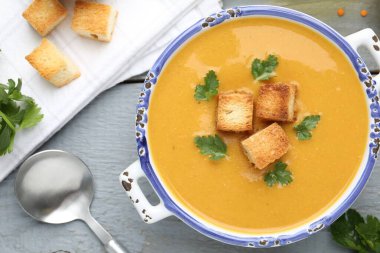 Lezzetli mercimek kremalı çorba. Gri ahşap masada kızarmış ekmeklerle servis ediliyor.