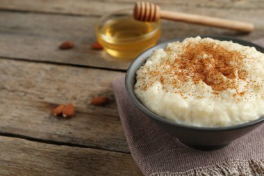 Tarçınlı lezzetli sütlaç, bal ve badem ahşap masada, yakın plan.