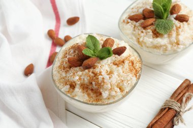 Tarçınlı lezzetli pirinç pudingi, beyaz ahşap masada nane ve badem, yakın plan.