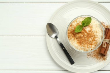 Tarçınlı lezzetli sütlaç, beyaz ahşap masada nane ve kaşık, üst manzara. Metin için boşluk