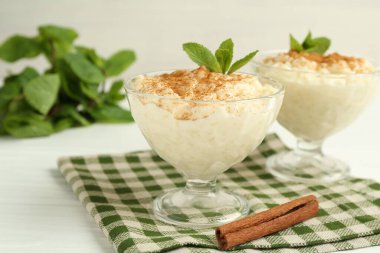 Tarçınlı lezzetli pirinç pudingi ve beyaz ahşap masadaki cam tatlı kaseleri, yakın plan.