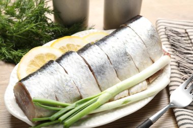 Limon dilimli lezzetli ringa balıkları, yeşil soğan ve ahşap masada dereotu, yakın plan.