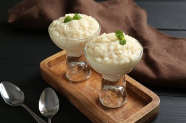 Nane şekerli lezzetli sütlaç ve siyah ahşap masada kaşıklar, yakın plan.