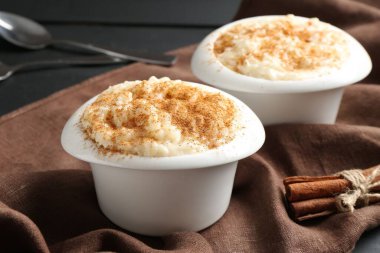 Tarçınlı lezzetli sütlaç ve siyah ahşap masada kaşıklar, yakın plan.