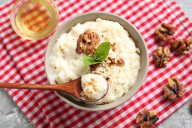 Lezzetli sütlaç kasede, ceviz, nane, bal ve kaşık masada.