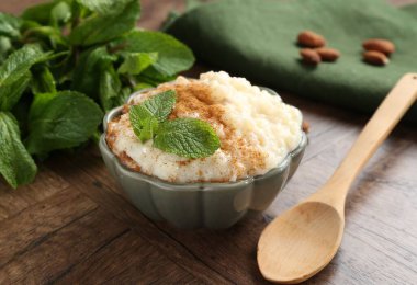 Tarçınlı, naneli, bademli ve ahşap masadaki kaşıklı lezzetli sütlaç.