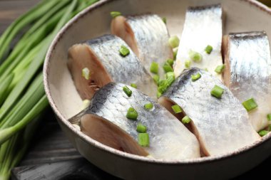 Siyah ahşap masada servis edilen taze soğanlı lezzetli ringa balıkları.