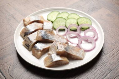 Lezzetli ringa balıkları, soğan ve salatalık dilimleri ahşap masada, yakın plan.
