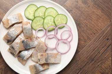 Lezzetli ringa balıkları, soğan ve ahşap masa üzerindeki salatalık dilimleri, üst manzara. Metin için boşluk
