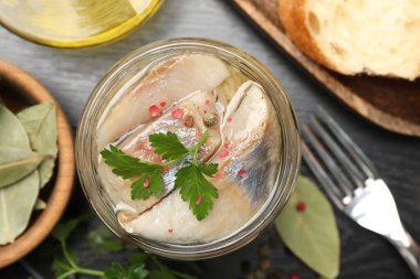 Kavanozda baharat ve siyah masada ekmek olan lezzetli ringa balıkları.