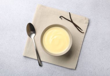 Lezzetli vanilyalı puding kasede, kapsüller ve kaşık açık gri masada, düz yerde