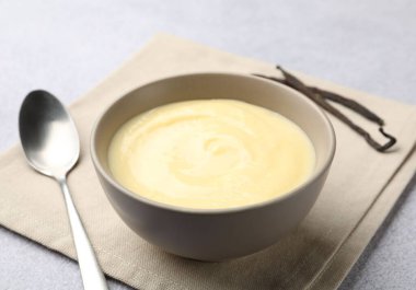 Lezzetli vanilyalı puding, kapsüller ve kaşık açık gri masada, yakın plan.