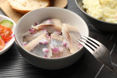 Siyah ahşap masada servis edilen soğanlı lezzetli ringa balıkları, yakın plan.