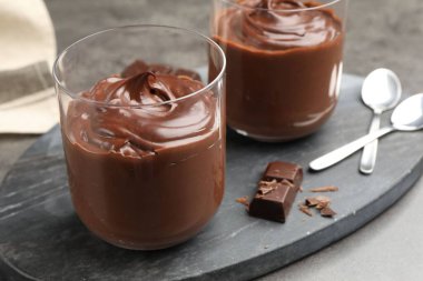 Lezzetli puding ve çikolata parçaları gri masada, yakın plan.