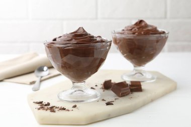 Tatlı kaselerinde lezzetli çikolatalı puding beyaz masada tuğla duvara karşı, yakın plan.